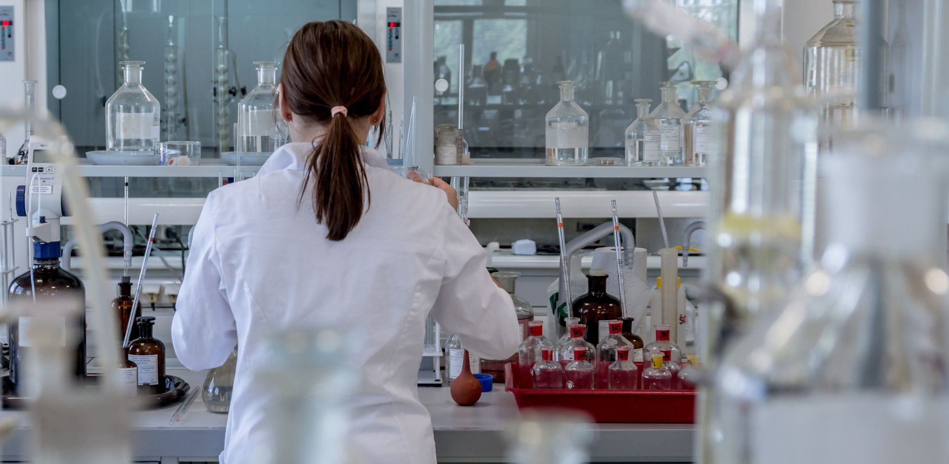 Giovane ragazza di spalle indossa un camice bianco all'interno di un laboratorio scientifico